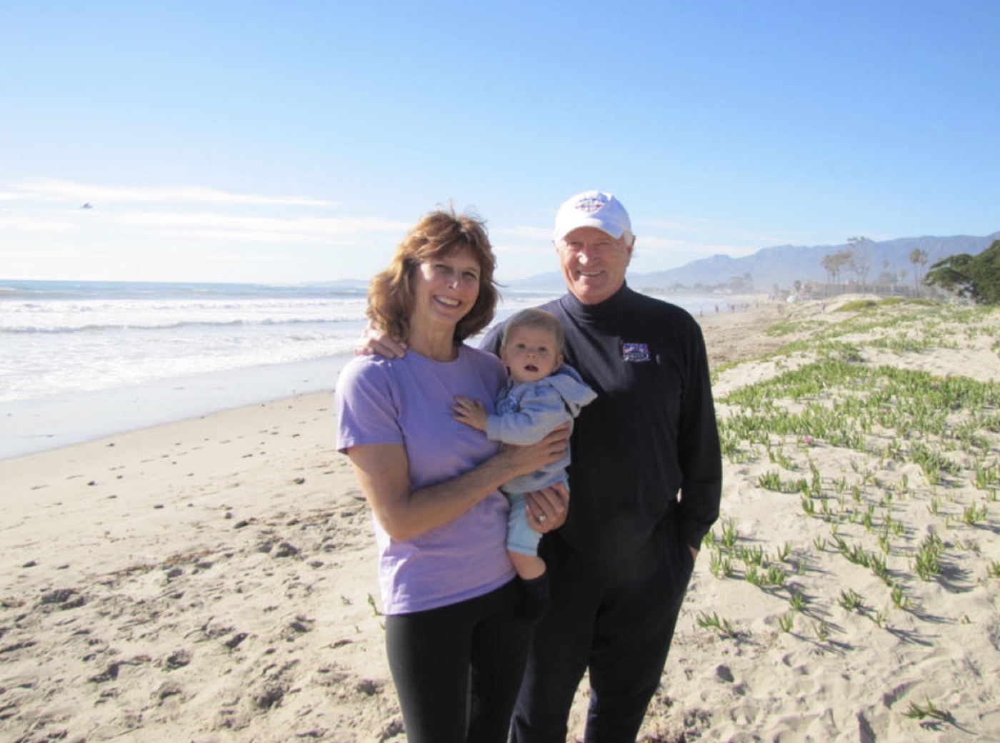 Bruce and Dana on the beach, holding a baby